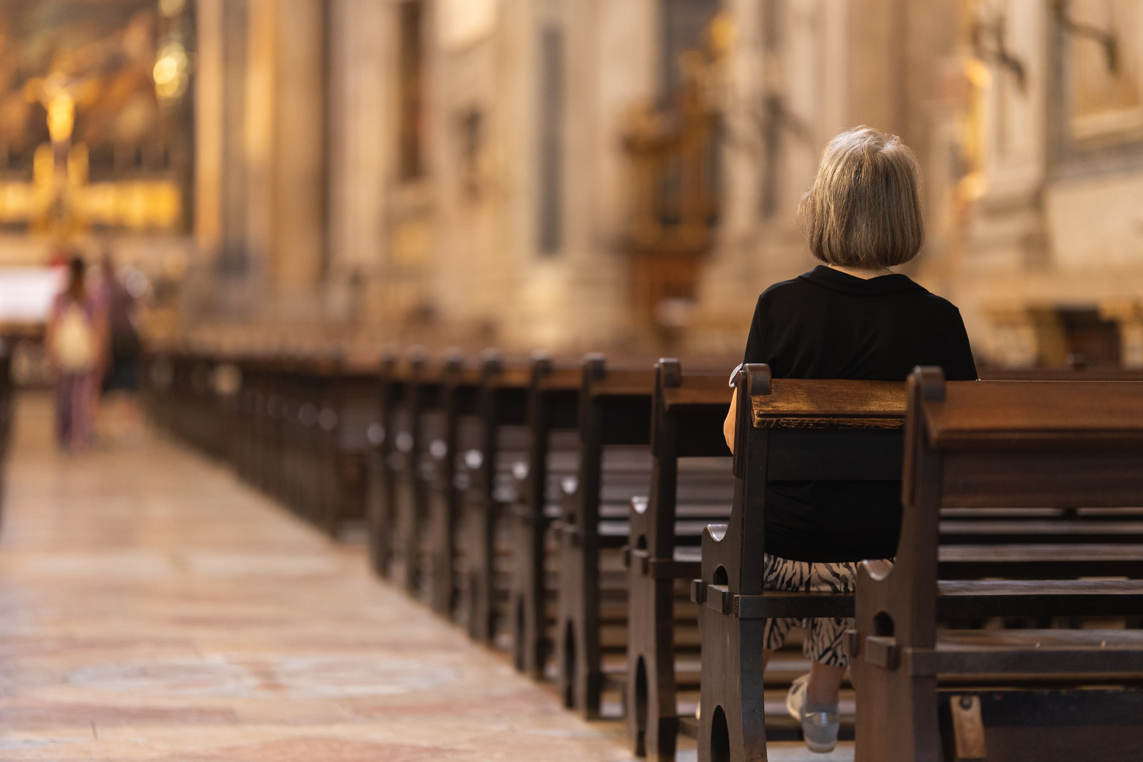 Frau sitzt allein nachdenklich in einer Kirchenbank